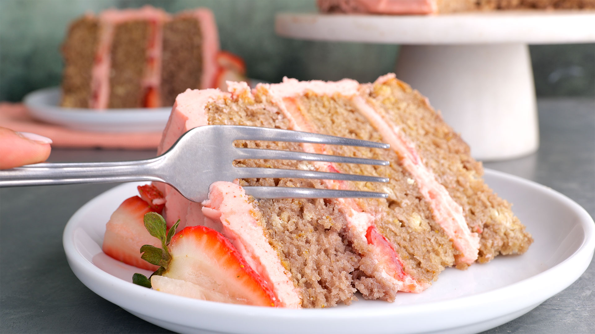 A slice of strawberry cake with a fork digging into it.